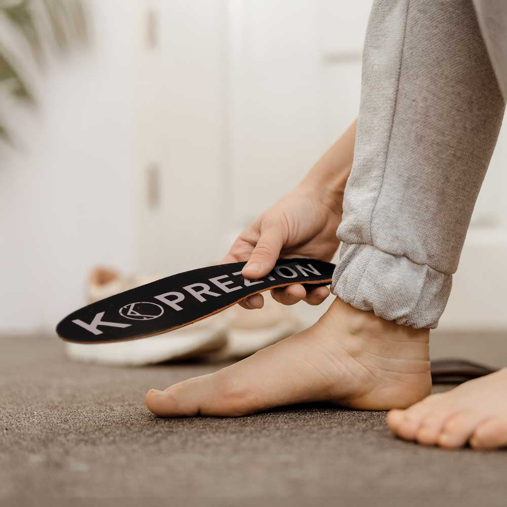 Person holding a black Koprezion insole beside their bare foot